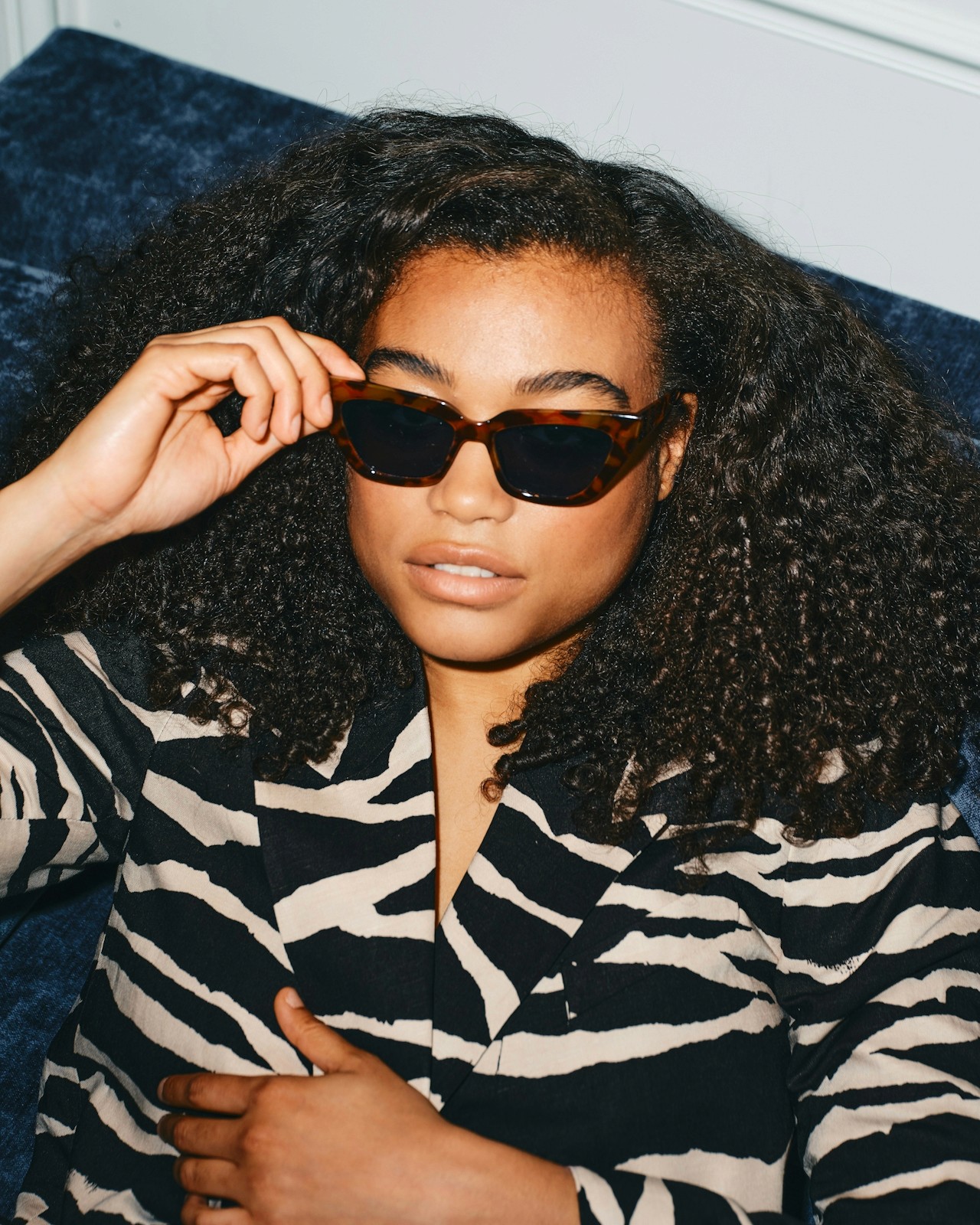 A woman wearing sunglasses and a patterned outfit, posing indoors.