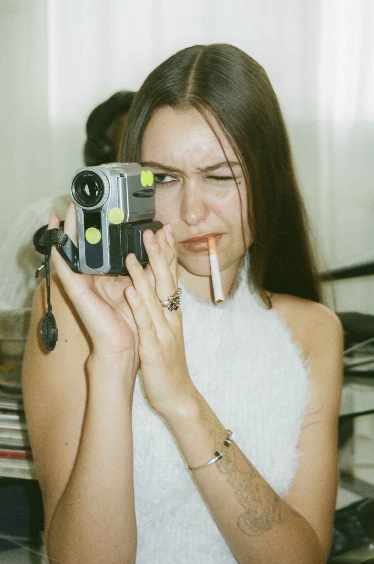 A woman holding a vintage camera while smoking a cigarette.