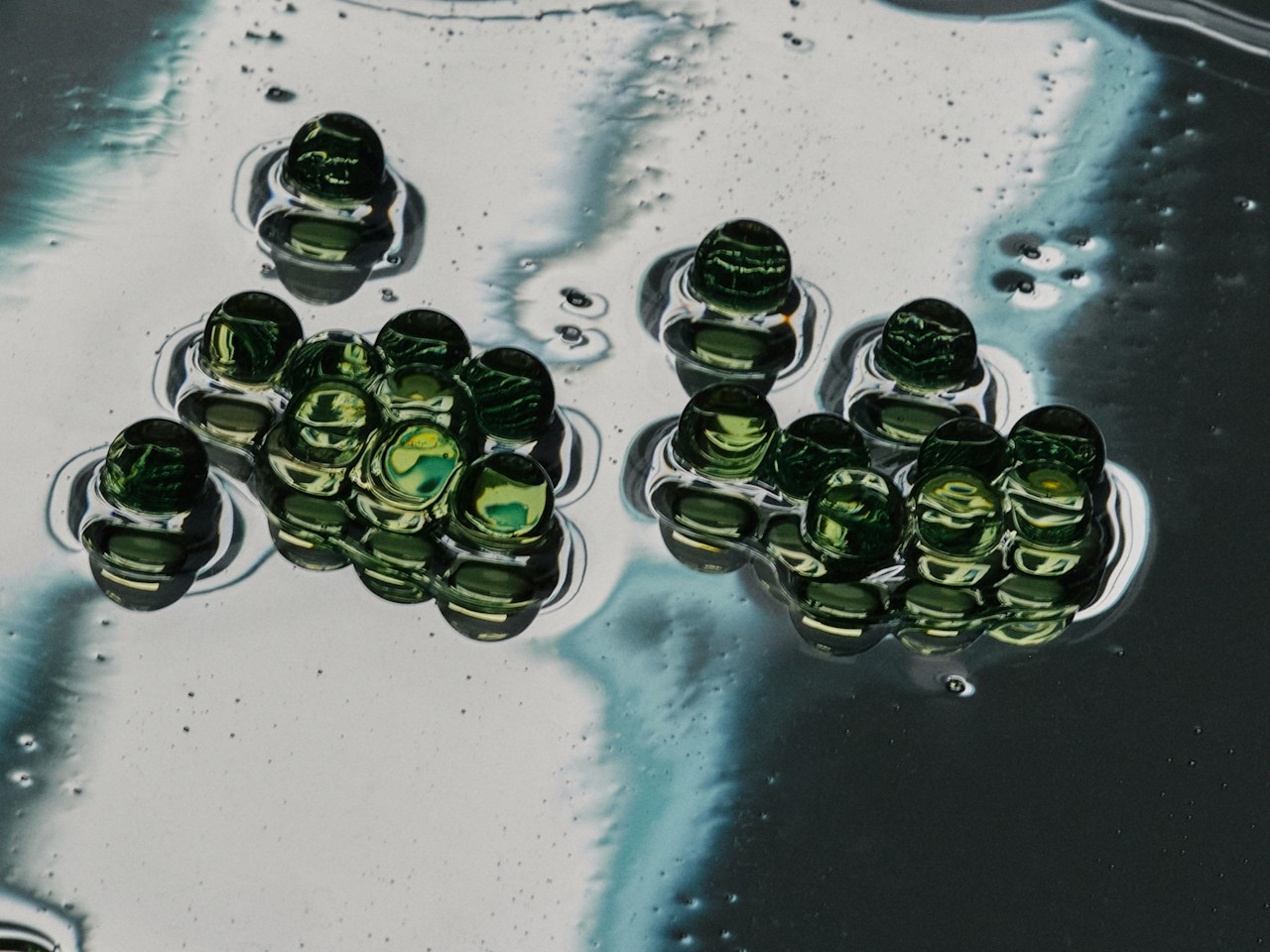 Green glass-like spheres clustered on a reflective liquid surface.