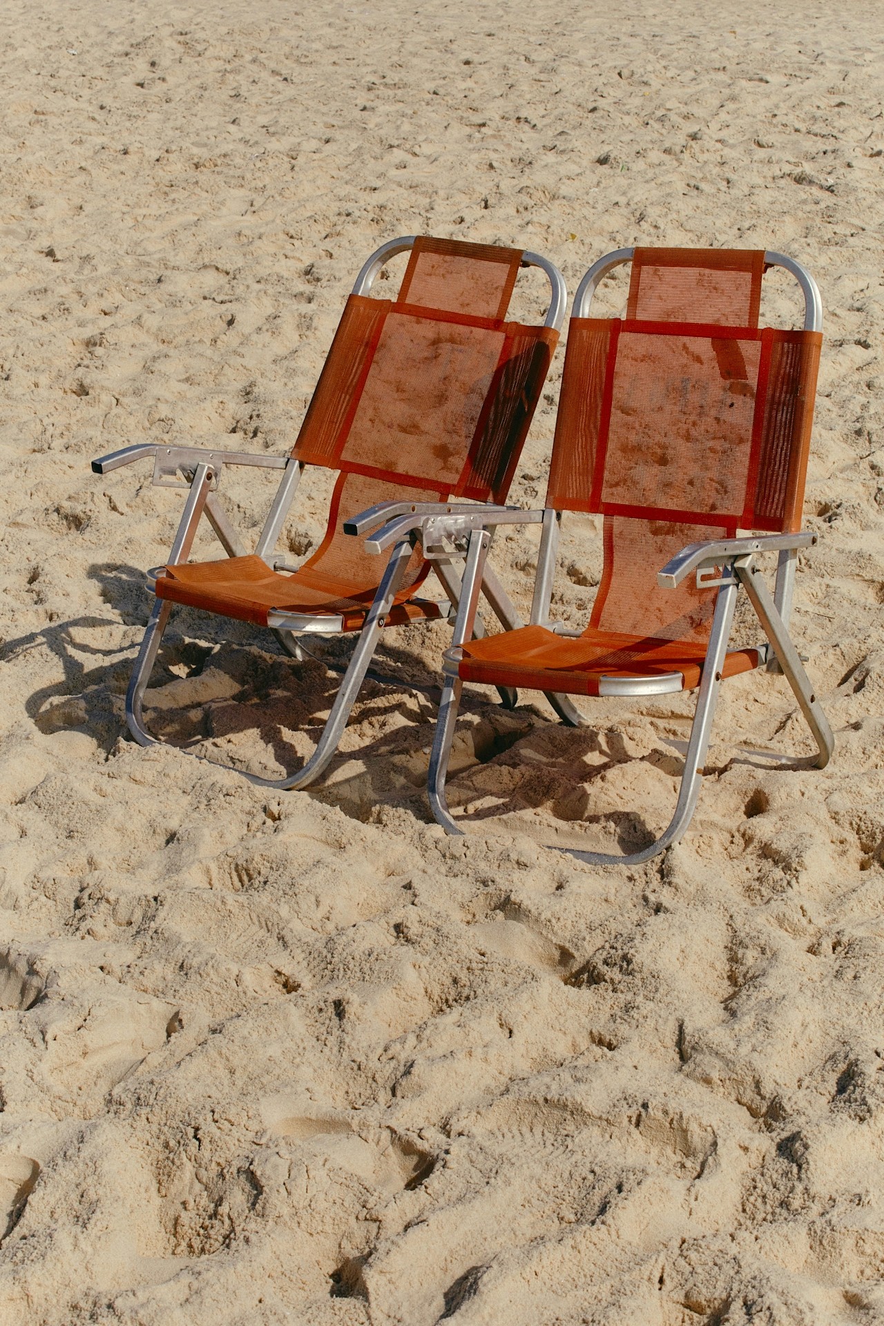 Two empty beach chairs placed on sandy ground.