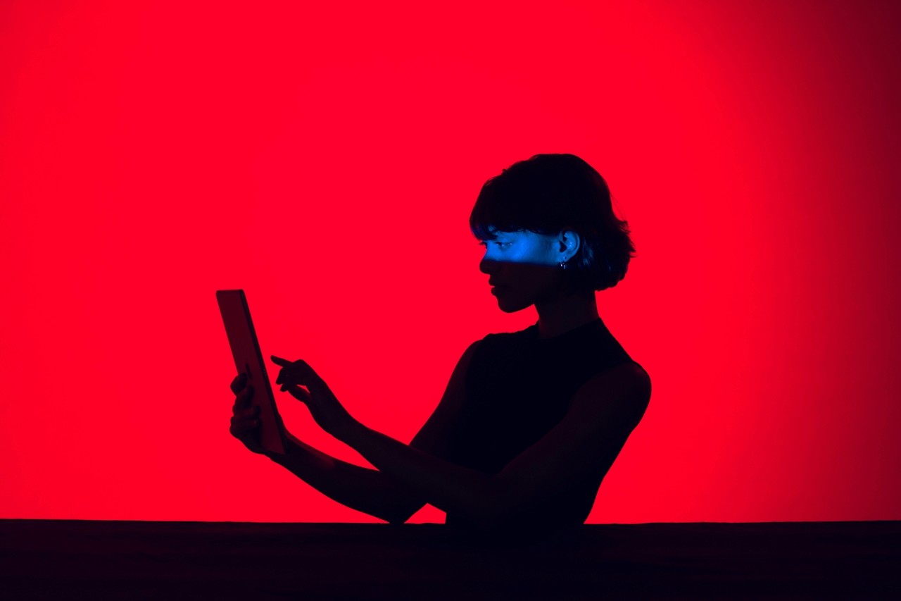 A woman in red lighting holding a tablet while getting filmed.
