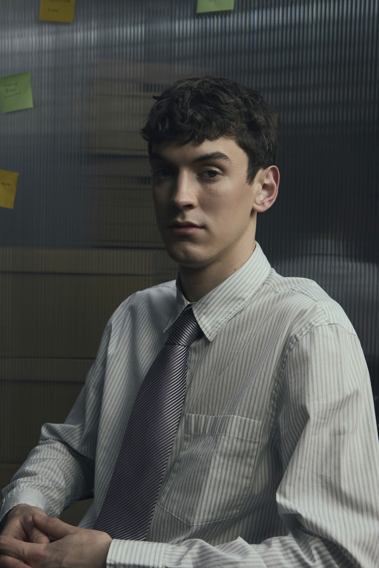 A young man wearing a striped shirt and tie, seated in an office setting.