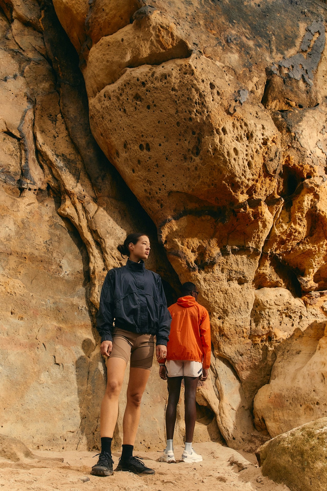 Two friends standing on a rock overlooking a mountain landscape.