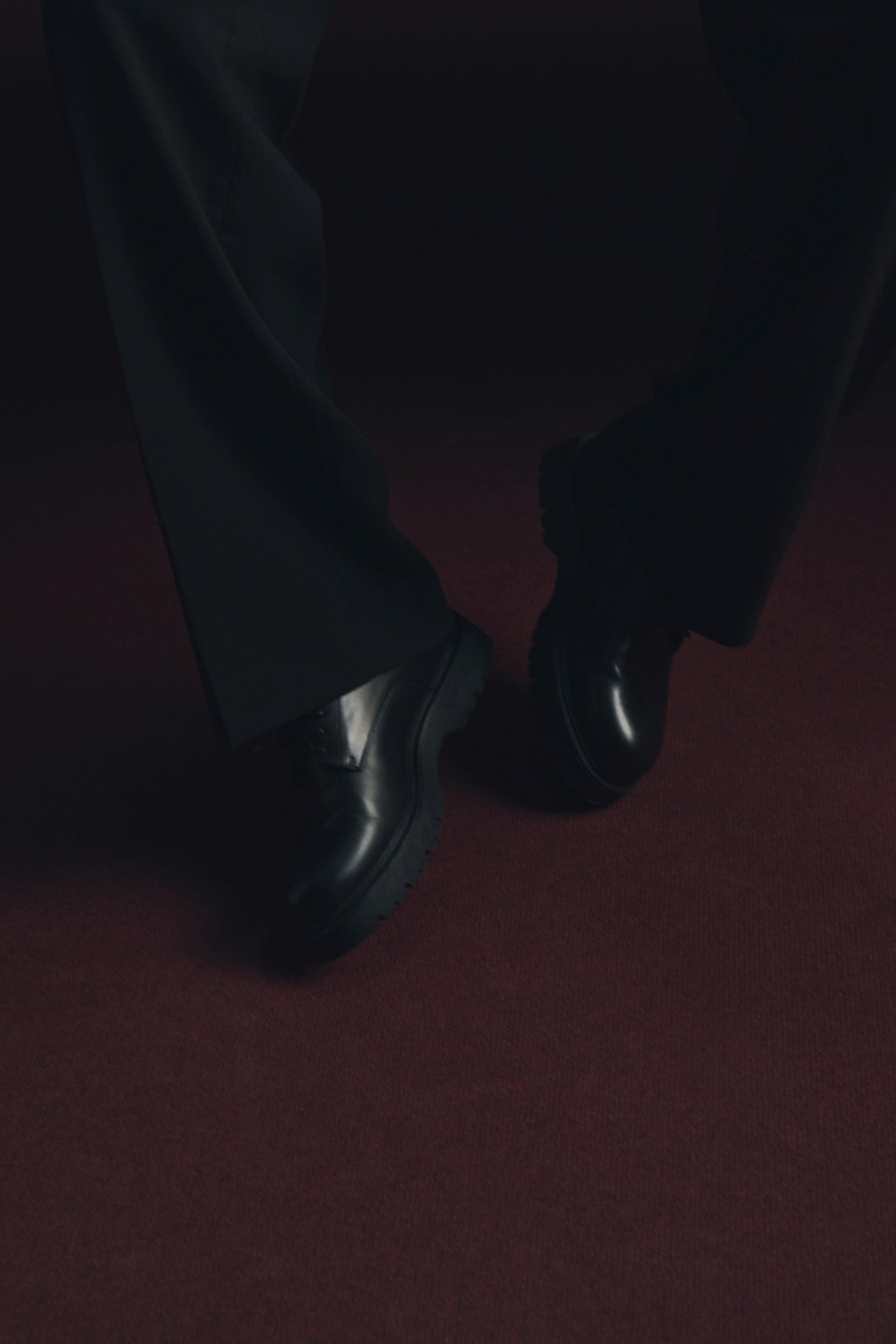 Black shoes worn on a maroon carpet.