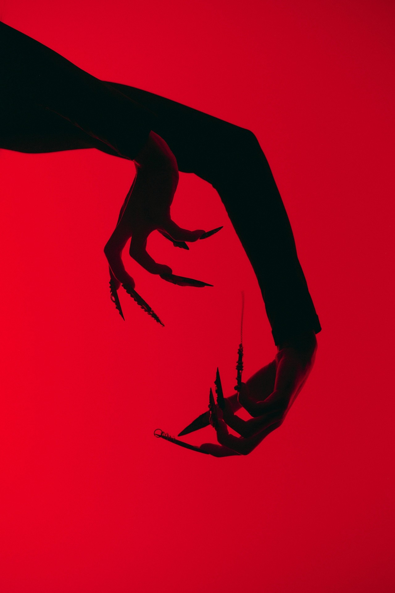An expressive hand gesture with elongated nails on a red backdrop.