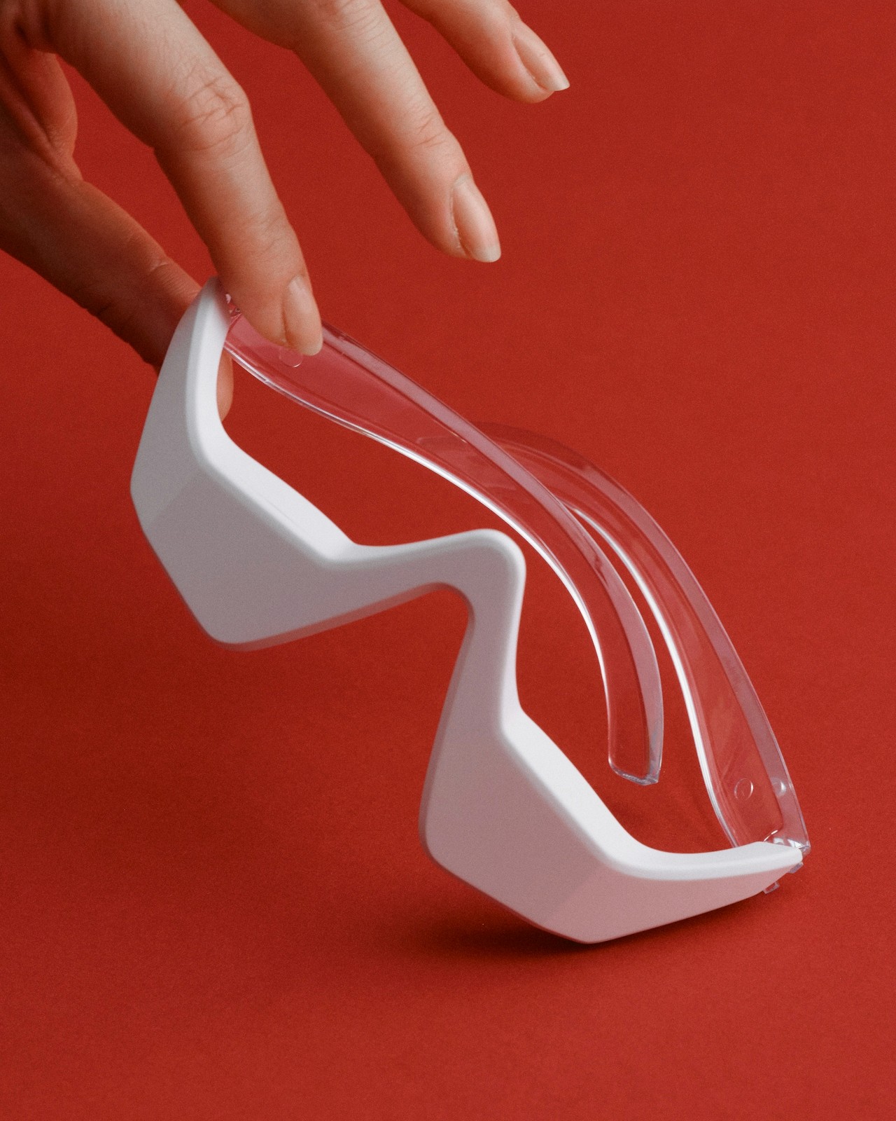 A hand holding modern white eyewear against a red background.