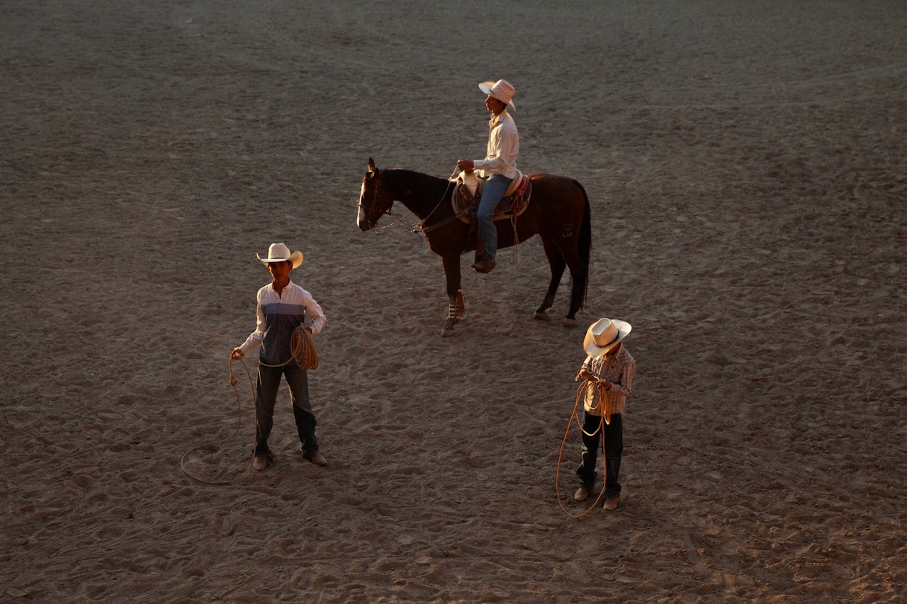 A group of cowboys preparing with ropes and a horse in an open arena.