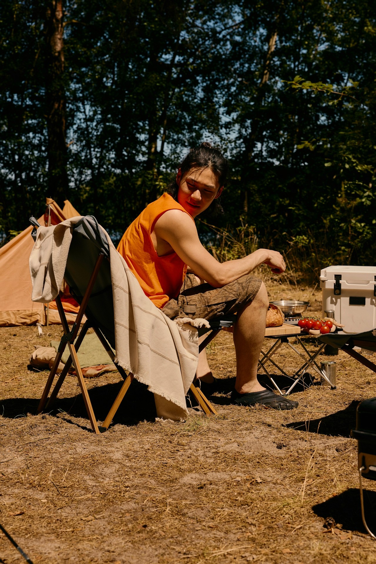A man in orange shirt seated on a chair among trees.