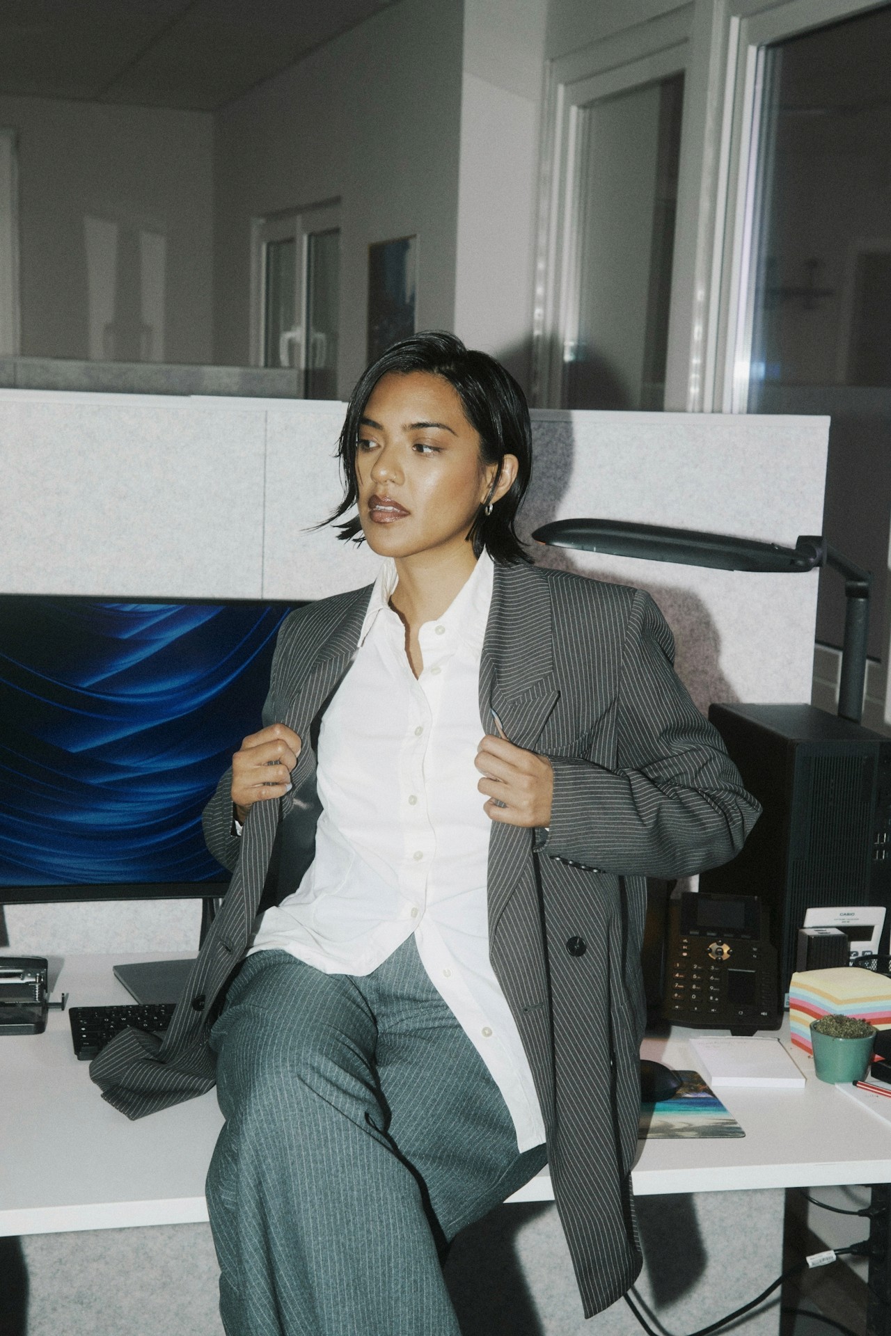 A woman adjusting her blazer while sitting in an office workspace.