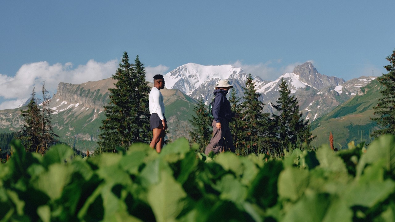 Two people walking through a green field in a mountainous landscape.