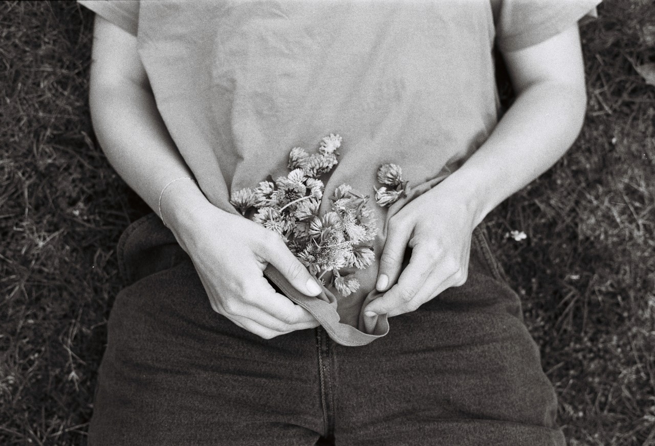 Hands holding small wildflowers gathered against the body.