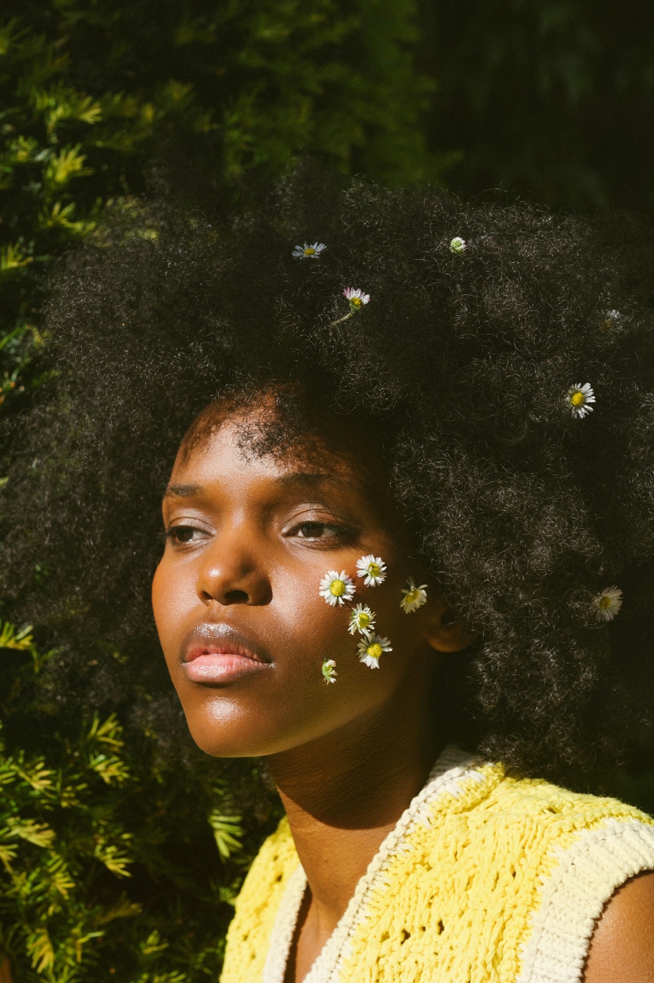 A woman with flowers placed on her face, photographed outdoors in natural light.