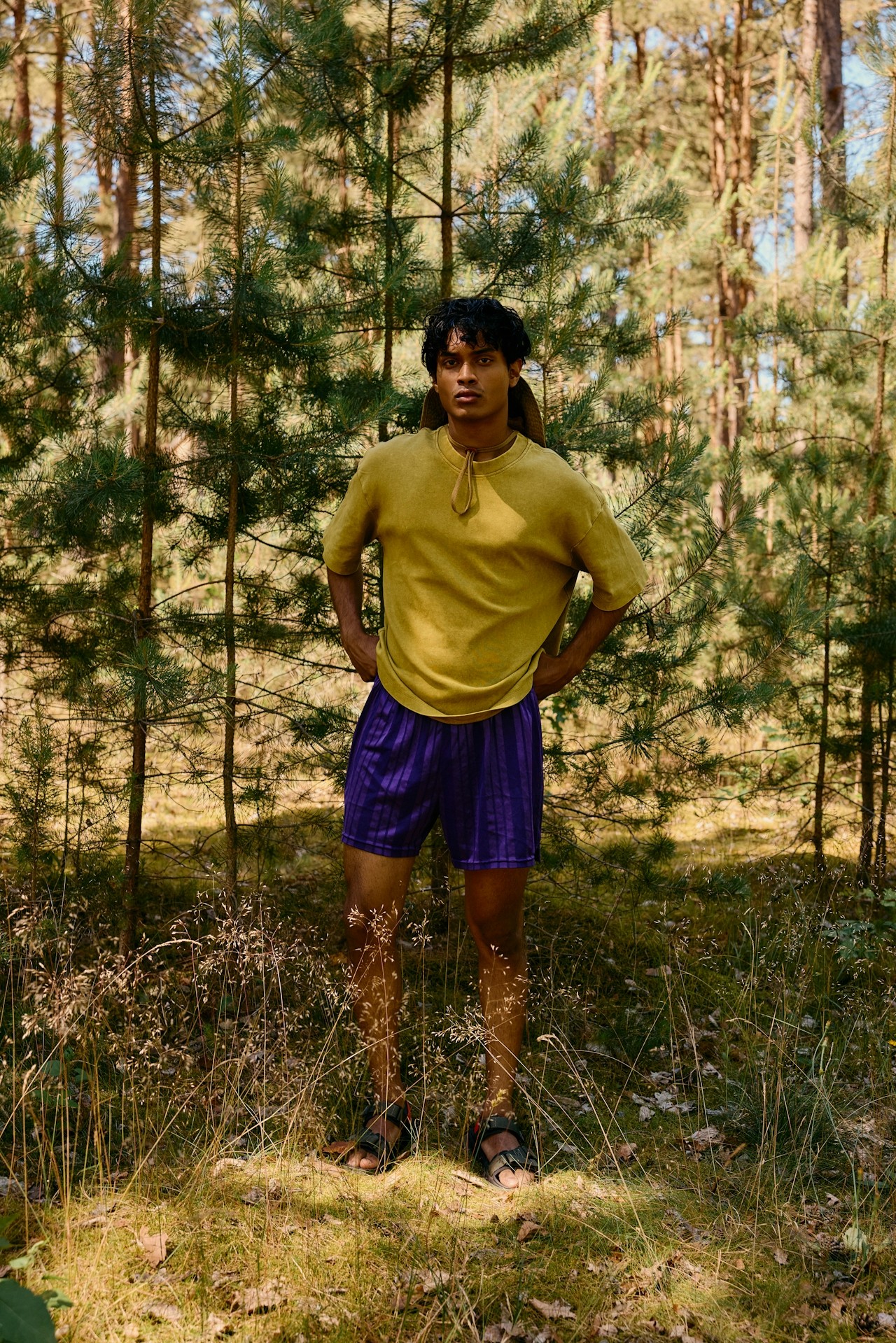 A man wearing a yellow shirt standing among trees in a forest.