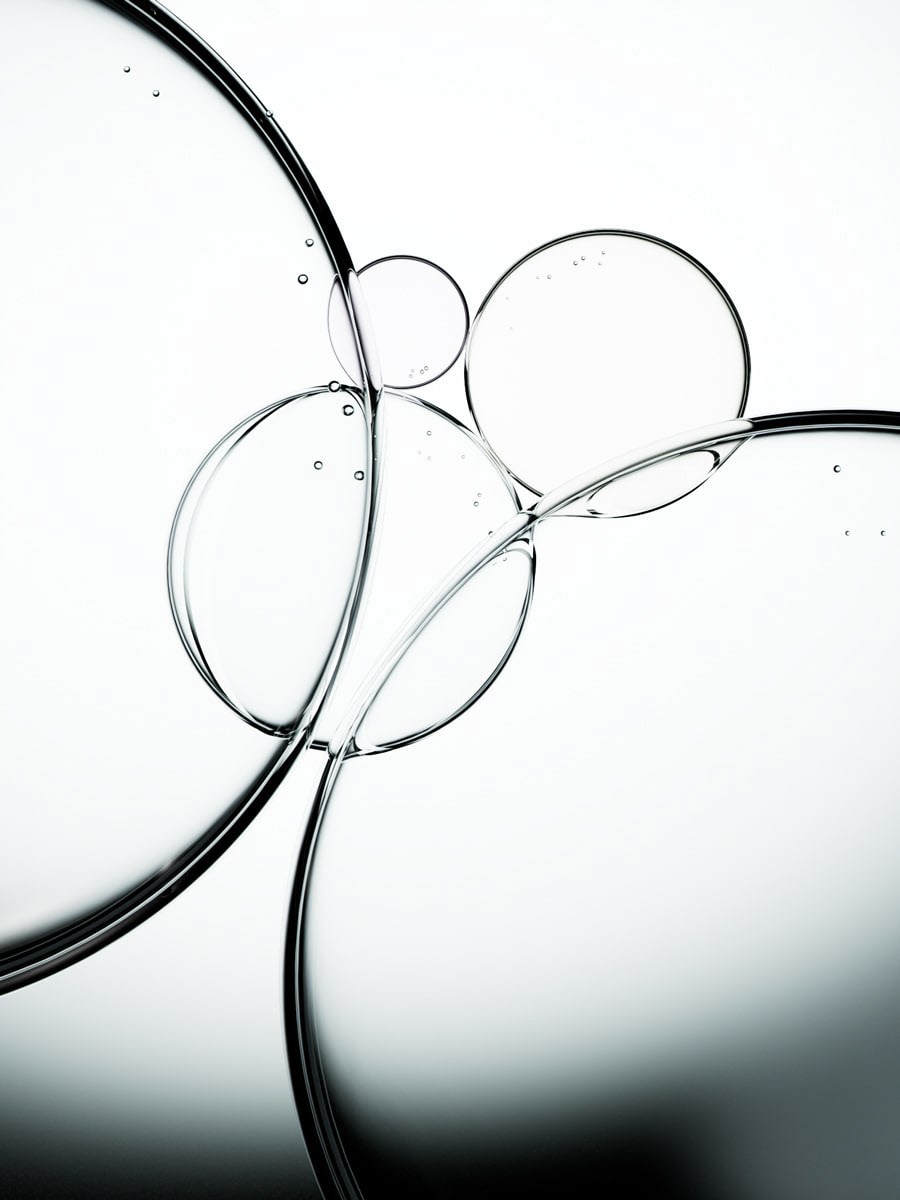 A crisp, high-key macro image of clear liquid bubbles or oil droplets of varying sizes, interconnected and floating against a stark white background. The composition emphasizes purity, transparency, and delicate forms, with subtle reflections showcasing the clean lines. This abstract visual is perfect for representing pure cosmetic formulations, hydrating serums, essential oils, or scientific advancements in beauty. It would lend a sophisticated and clean aesthetic to product features or banners on a **Liqua Premium Ecommerce template**, conveying a sense of quality and innovation.