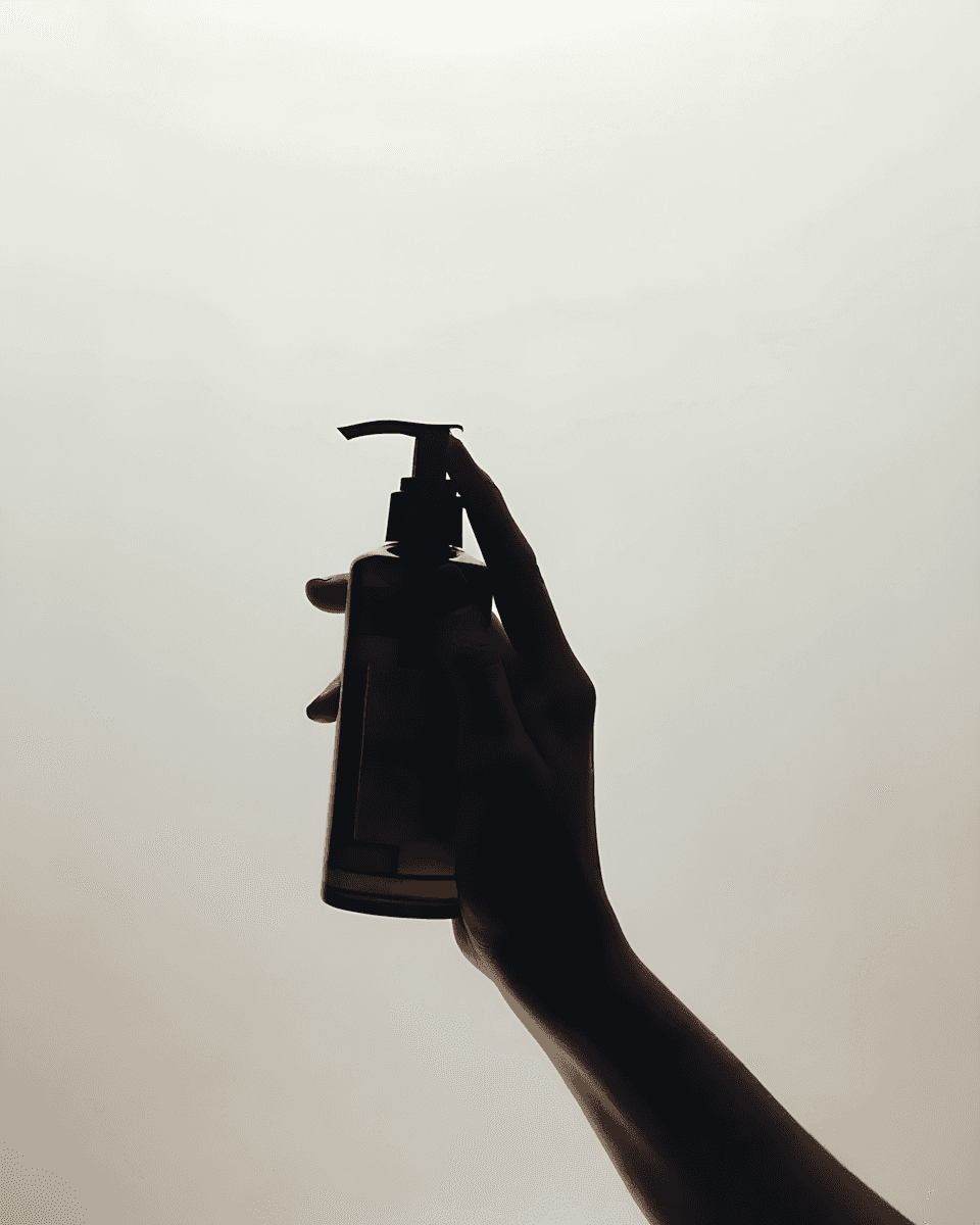 A dramatic silhouette of a hand holding up a pump dispenser bottle against a bright, hazy background. The high contrast emphasizes the product's form and the action of dispensing, suggesting effective and easy use. This visual is suitable for promoting a variety of liquid products, such as hand soap, lotion, shampoo, or sanitizer. It can effectively be used on a **Liqua Premium Ecommerce template** to convey user experience and product accessibility.